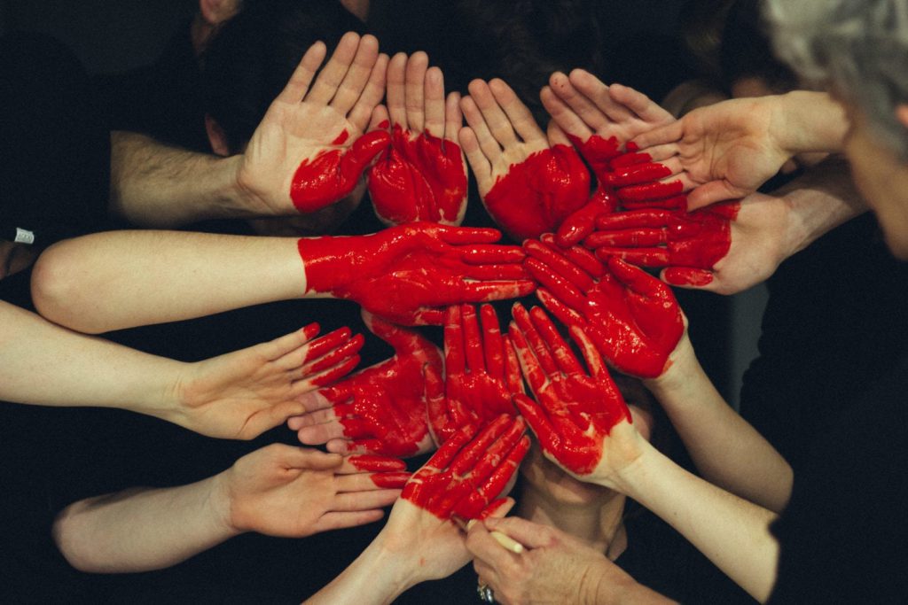 a shot of a few hands with palm facing forward and colored with red paint making a big heart shape