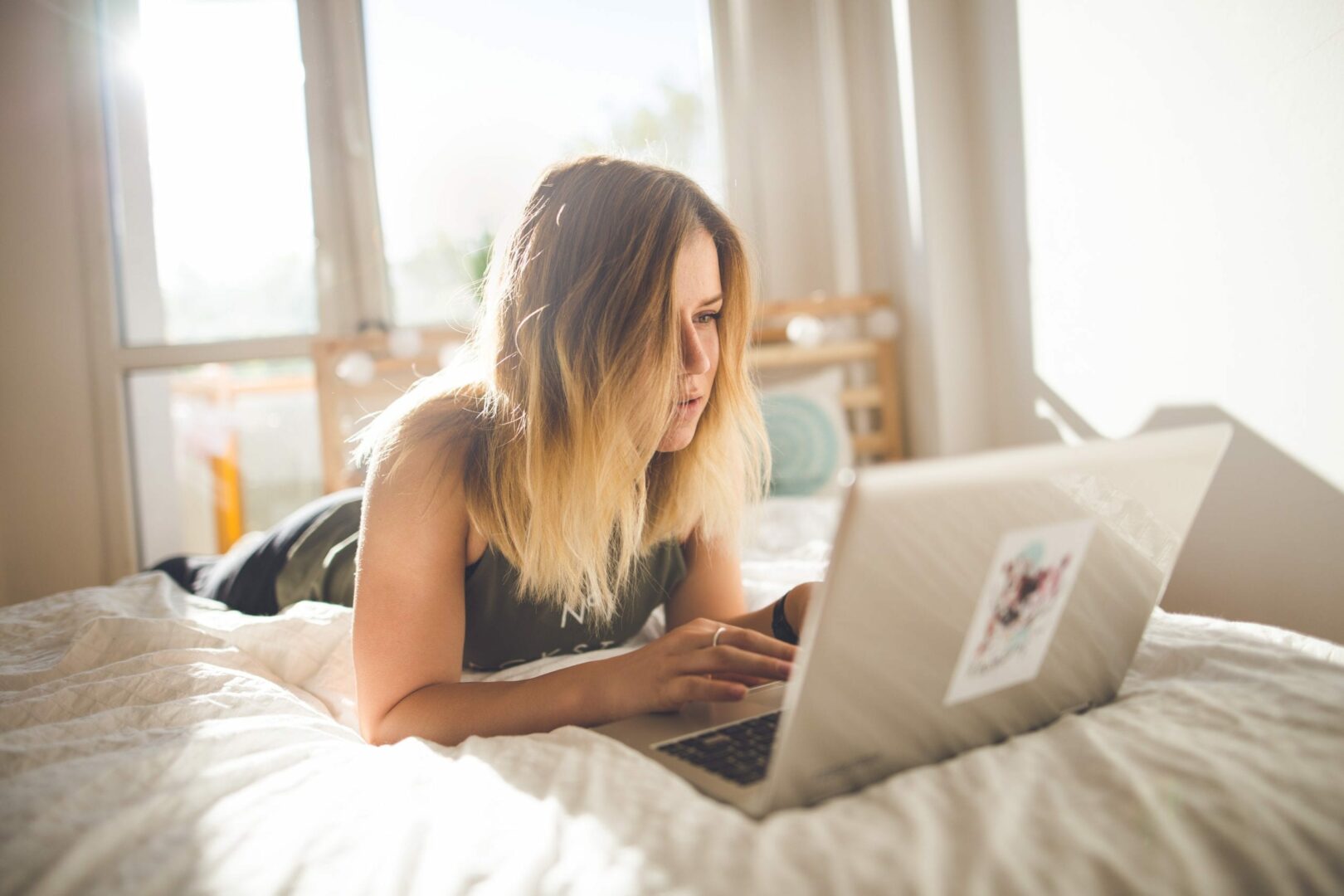 an image of a woman lying on her stomach on the bed while using a laptop