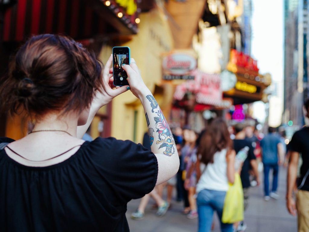 a shot of a woman from behind taking a shot of a busy road using her phone