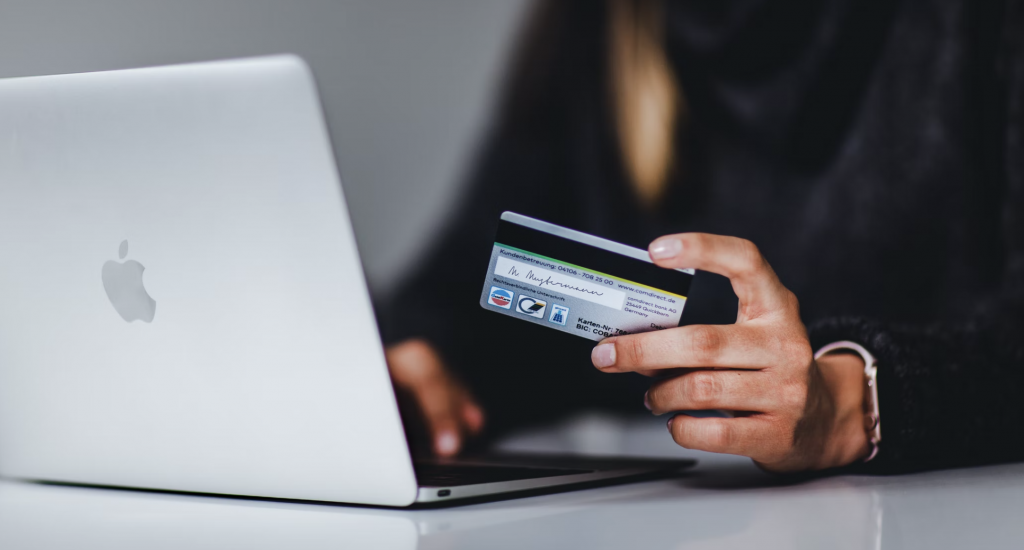 a shot of a woman holding a credit card with the left hand and the right hand typing on the laptop in front of her