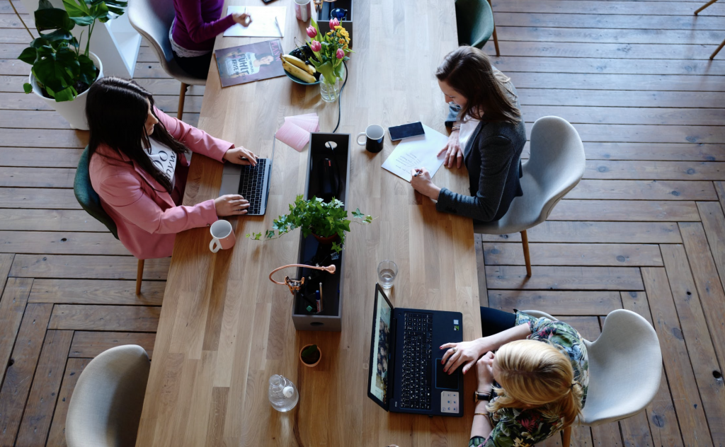 an aerial shot of a few women working at a wooden table in a brightly lit room