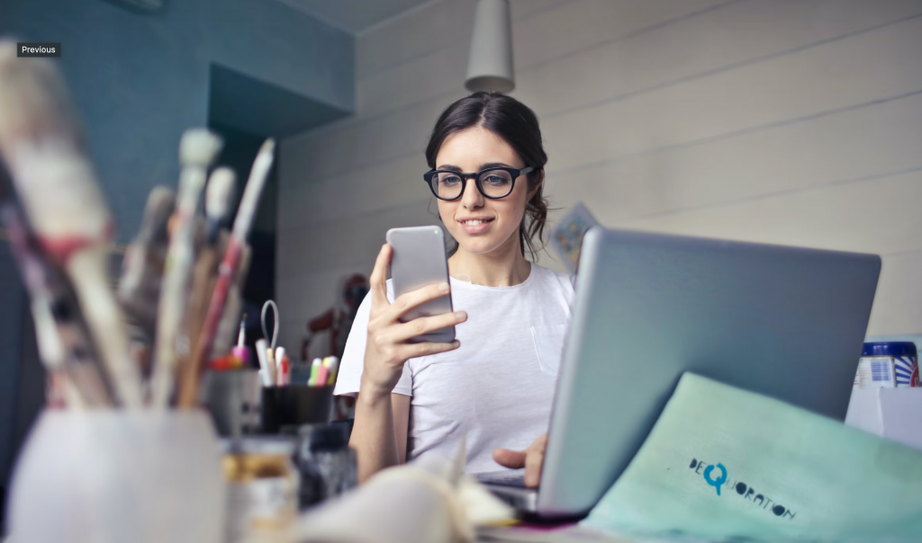 a shot of a woman using her phone with the right hand with a laptop on her lap held by the left hand