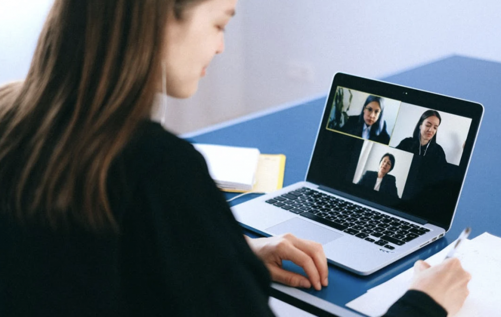 a shot of a woman on a video conference looking at a laptop with the screen showing the participants of the conference