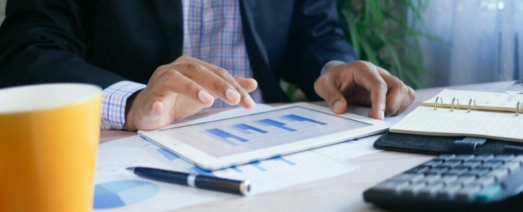 a shot of a man using a tablet on a table with a bar chart on the screen